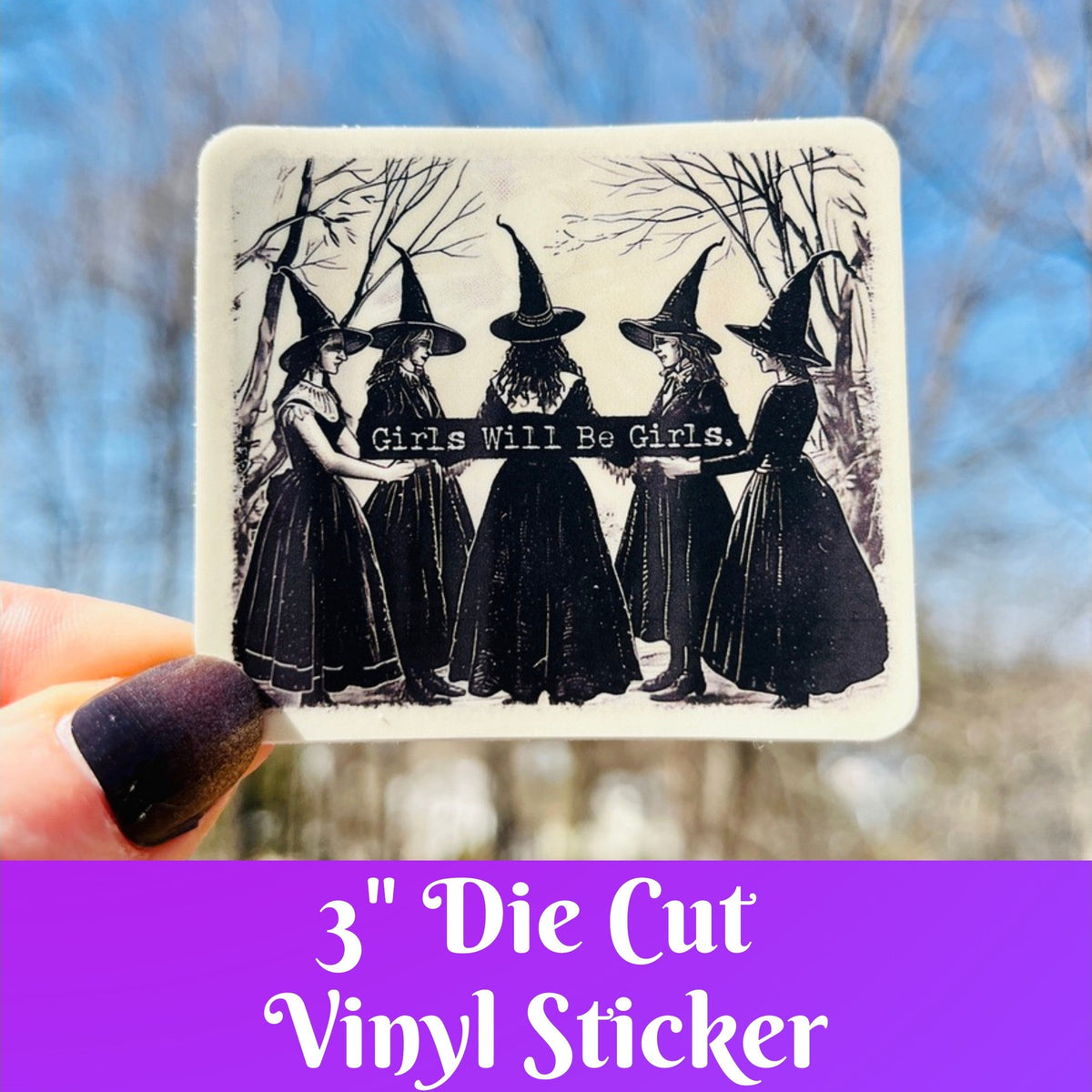 A hand holds a square die-cut vinyl sticker featuring a black-and-white illustration of five witches in pointed hats with the text 'Girls Will Be Girls.' The background is an outdoor scene with blurred trees and blue sky, and a purple banner at the bottom reads '3" Die Cut Vinyl Sticker'.
