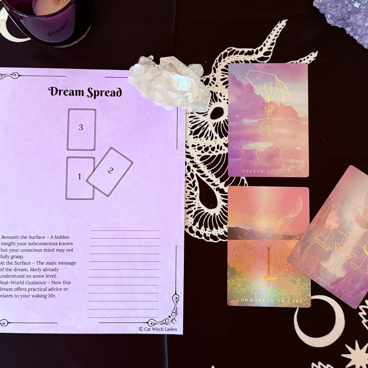 A tarot card reading kit laid out on a dark patterned cloth, featuring a printed 'Dream Spread' worksheet, three pastel iridescent oracle cards, a white crystal, and a purple glittery orb.