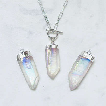 Three silver-toned crystal point pendants on a silver chain, displayed on a white marble surface. The crystals have an iridescent, milky white appearance with subtle pastel rainbow reflections.