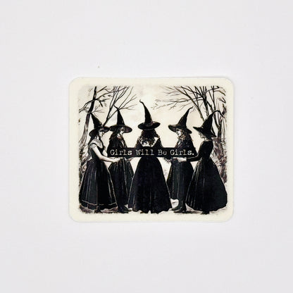 A square sticker with rounded corners featuring a vintage black and white illustration of five girls in witch hats holding a banner that reads 'Girls Will Be Girls.' against a light gray background.