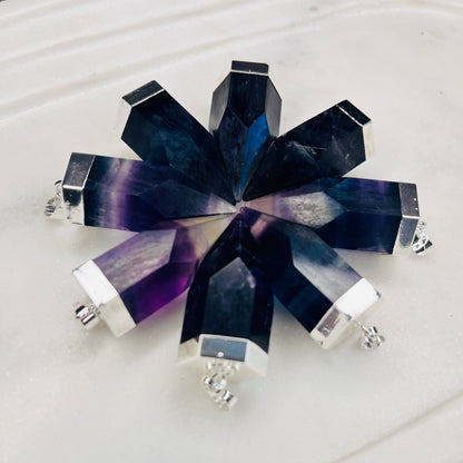 A faceted crystal brooch in a starburst shape, featuring dark blue and purple agate-like segments with polished silver metal borders and posts, displayed on a light textured surface.