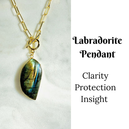 A gold chain necklace with a teardrop-shaped labradorite pendant, displayed on a white marble surface next to text that reads 'Labradorite Pendant Clarity Protection Insight'.