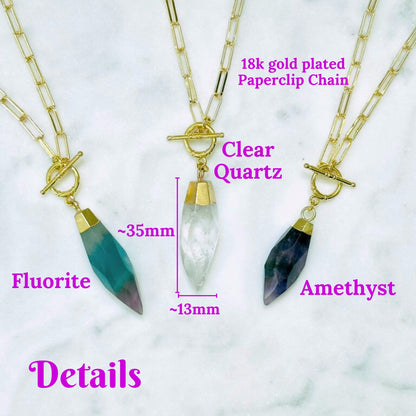 Three gold-plated paperclip chain necklaces with crystal pendants are displayed on a white marble background with pink text labels reading 'Fluorite', 'Clear Quartz', and 'Amethyst', plus size and detail callouts.