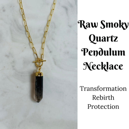 A gold chain necklace with a raw smoky quartz pendant, displayed on a white marble background with text on the right reading 'Raw Smoky Quartz Pendulum Necklace' and 'Transformation Rebirth Protection'.